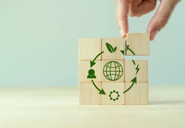 Drewniane klocki z ikonami zielonej energii układane przez dłoń na tle zielonego pokoju